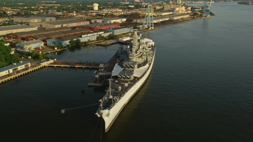Aerial footage of the USS New Jersey docked in Camden New Jersey during sunset over the Delaware River