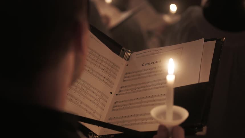 People are reading from a book holding candles