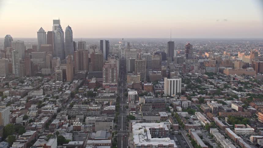 An aerial view of Philadelphias city skyline during sunset as the camera tilts up to reveal an urban South Philly neighborhood and downtown area