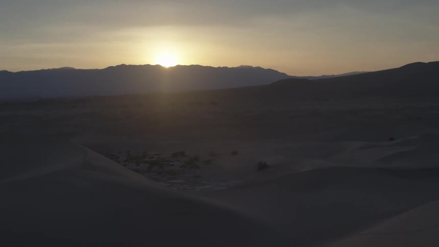 The sun sets behind mountains at the edge of a desert