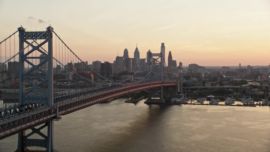 A breathtaking aerial view of the Benjamin Franklin Bridge crossing the Delaware River while flying towards the Philadelphia skyline during a beautiful sunset