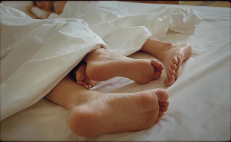 Mans feet touch womans feet lying in bed in bedroom