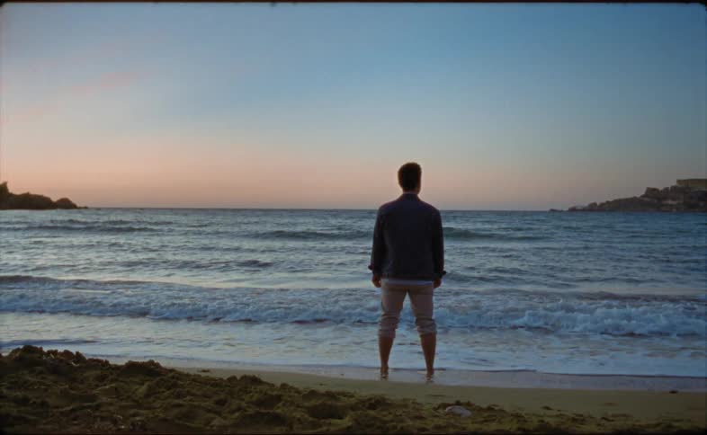 Man standing on the beach with his feet in the water while gazing at the horizon at sunset