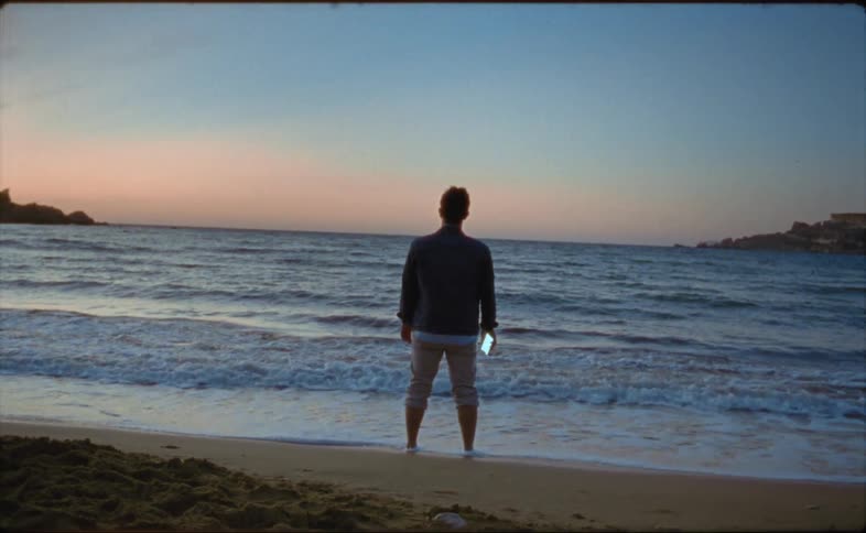 A man is standing at the beach while the sun is setting