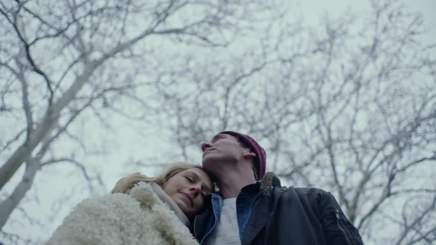 A man pulls his girlfriend closer for a hug while standing outside as it snows