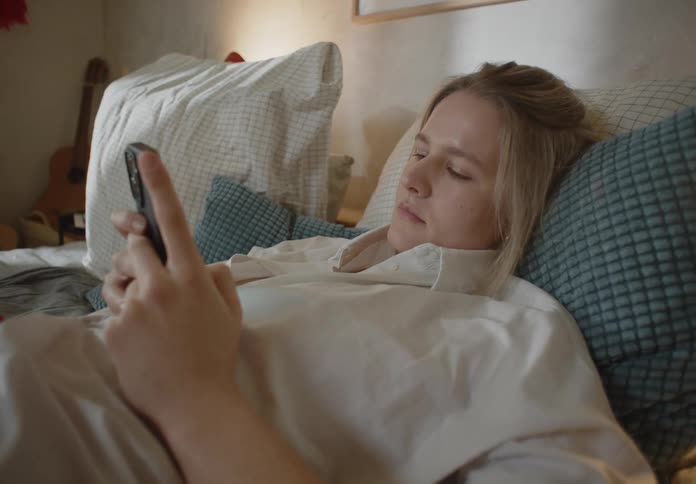 A woman scrolls through her phone while lying in bed