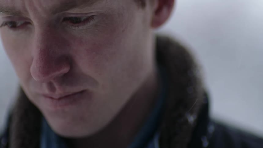 A young white man is standing outside in the snow