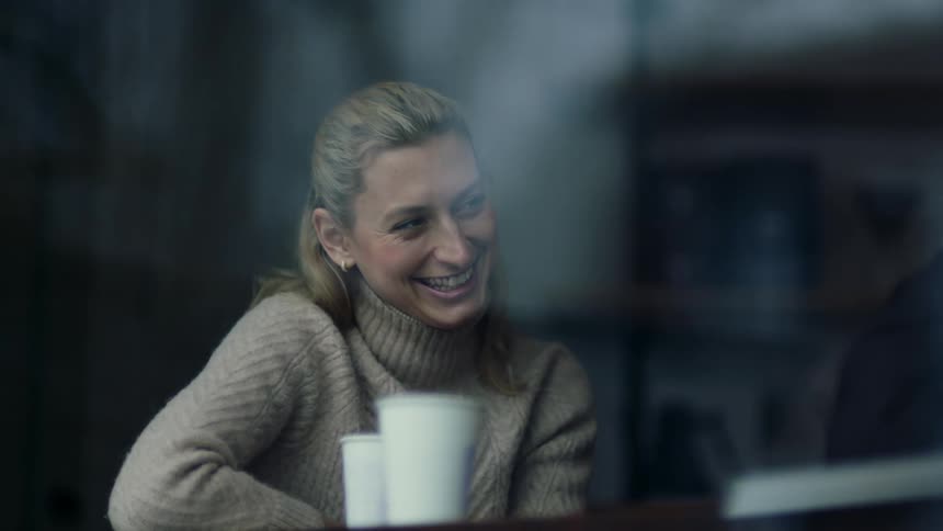 A young woman is talking to a friend and drinking coffee