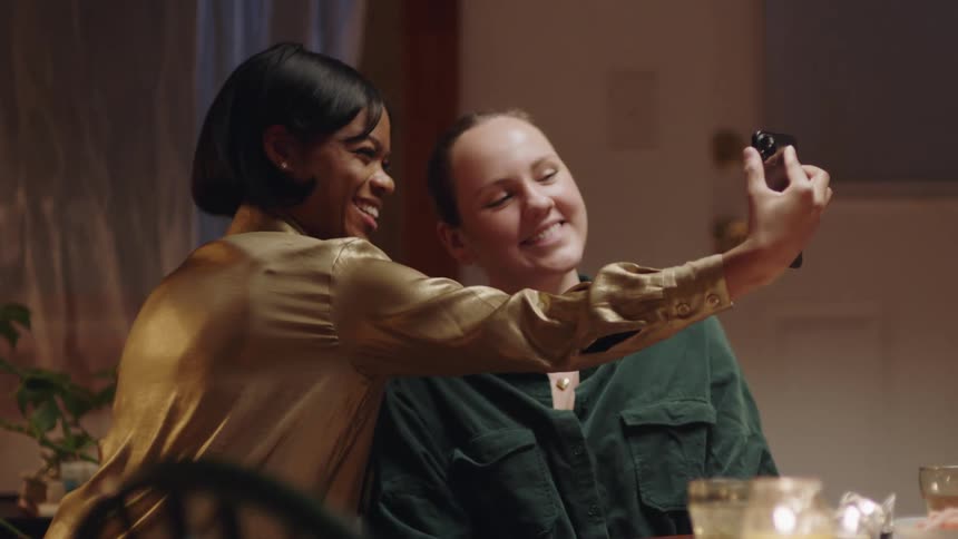 A woman is standing next to her friend as she holds out her phone and takes a selfie of them together