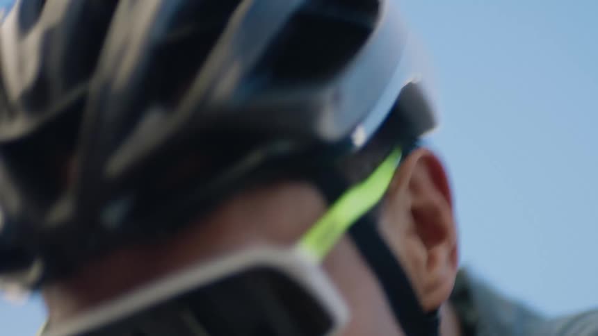 A man is wearing a cycling helmet and sun goggles as he pedals his bike