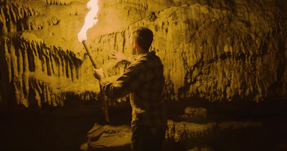 Man holding torch touches cavern wall