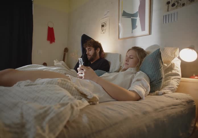 A man and woman laying down in bed the woman on her phone and the man reading a book