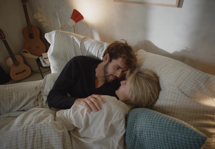 Couple lying in bed touches and looks into each others eyes in bedroom