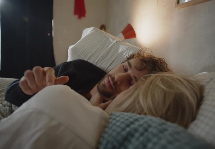 Couple lying in bed touches and looks into each others eyes lovingly in bedroom