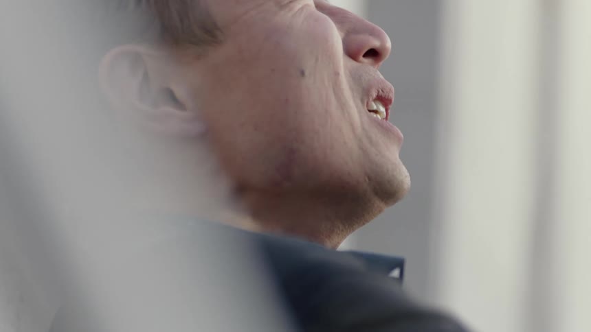 A man sits down and promptly takes off his helmet and takes many deep breaths to calm down