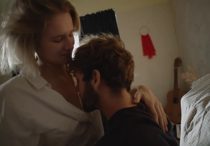 A man and woman kiss and cuddle sitting on a bed