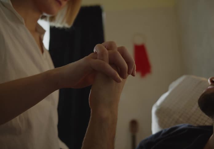 Woman and man hold hands while he reclines