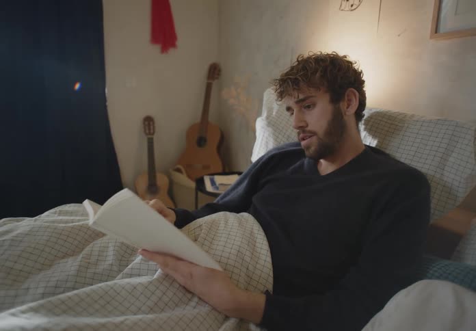 A man reads a book while resting in bed during the day