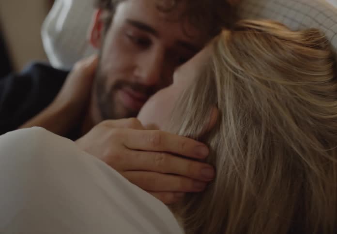 A young couple is laying in bed together around the morning time