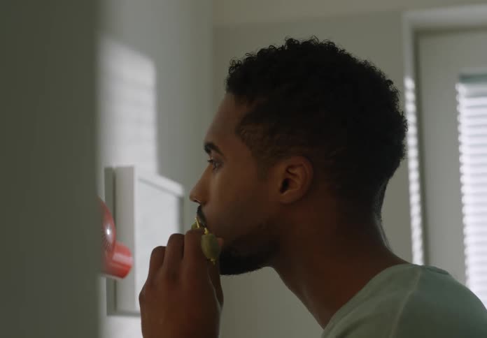 Man moves small roller over his cheeks while looking into mirror in bathroom