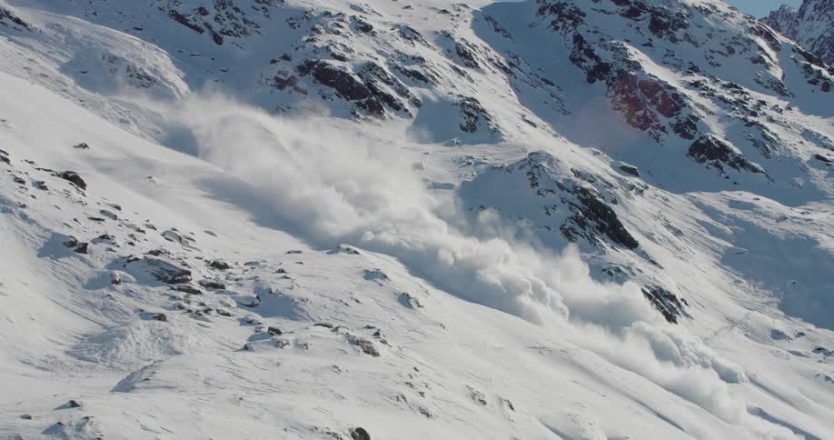 Snow rolling down a mountain slope covering rocks and creating a cloud