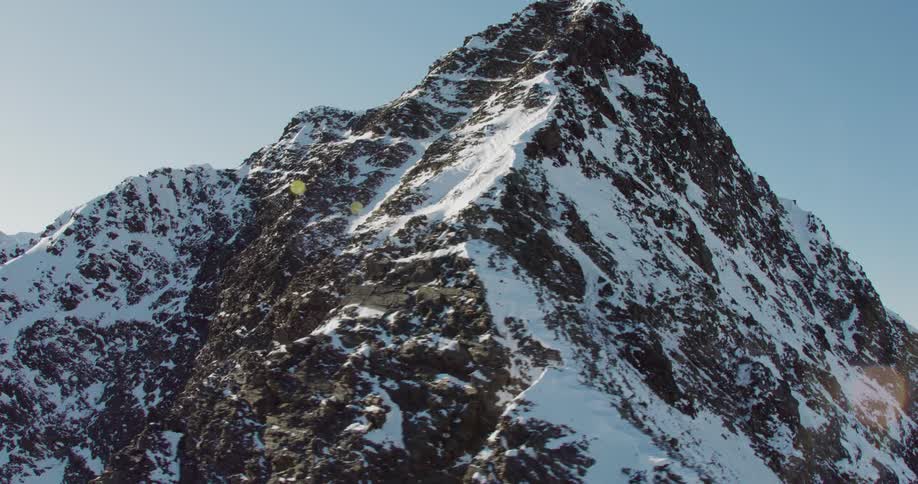 Aerial footage of a mountain peak covered by patches of snow shot on a sunny day