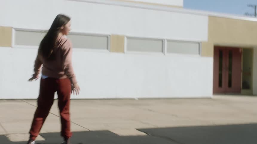 A teen girl with long hair riding a skateboard on a city street
