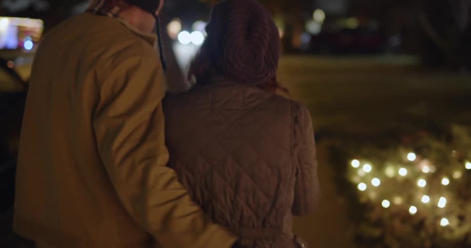 A couple man and woman walk together on the city street at night talking and carrying some christmas gifts