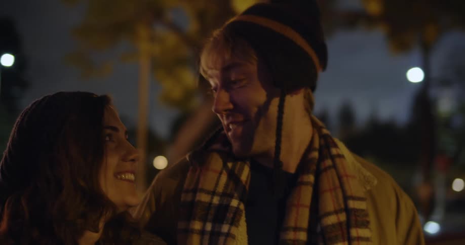 Couple talks and carries gifts while walking past homes decorated with christmas lights at night