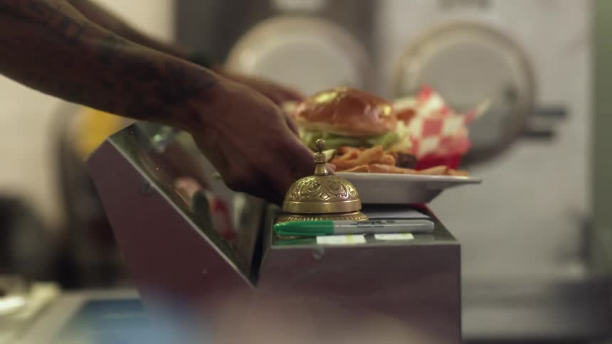 The cook in a fast food restaurant places an order of burger and fries on the counter top and rings a bell then the server picks the order up