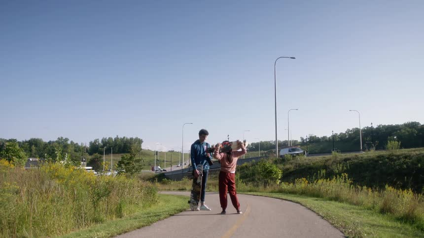 A girl and boy standing talking to each other holding skateboards on a walkway
