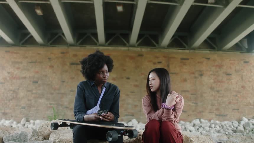 Two women sitting together talking under a bridge