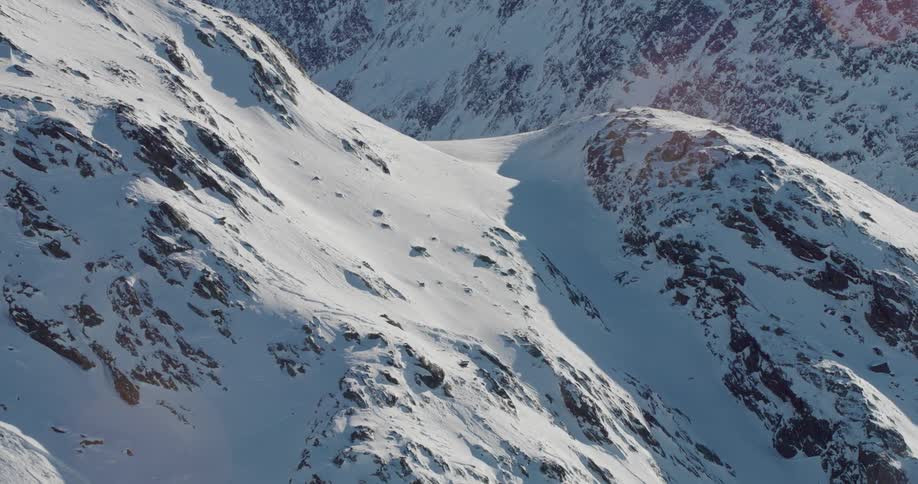 Sun glares over snow covered mountains casting shadows