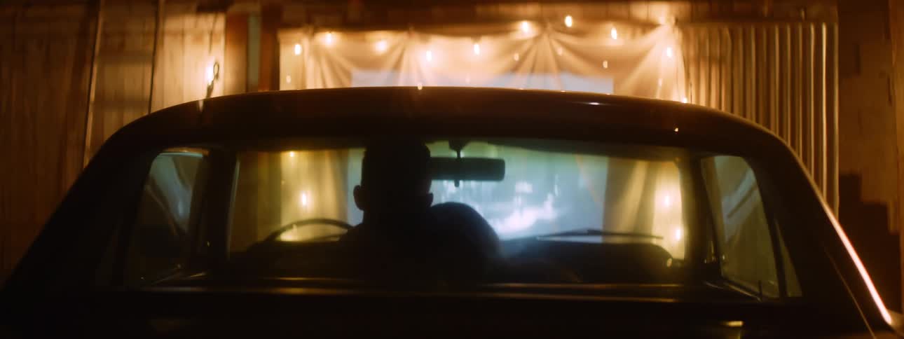 Couple cuddle while sitting in car watching image projected onto fabric