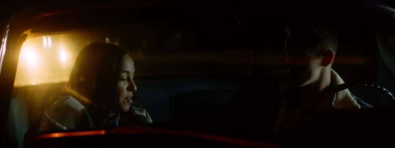 Man and woman sit in car looking at each other smiling at night