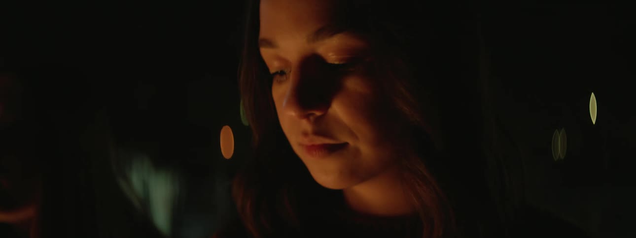 Woman with brown wavy hair sits next to bonfire touching her hair at night