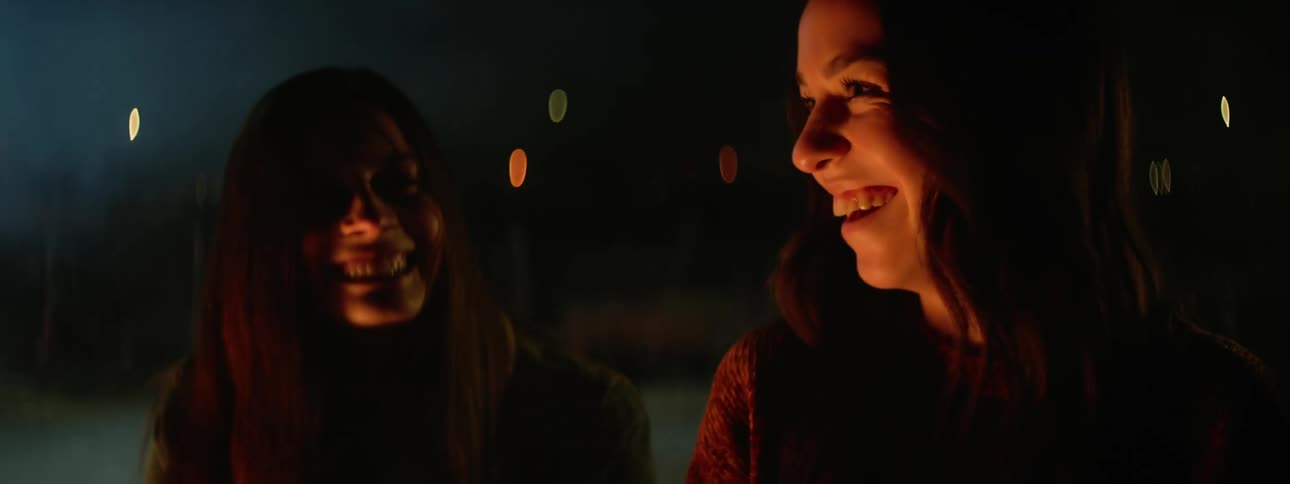 Two friends laugh while sitting around a fire outside