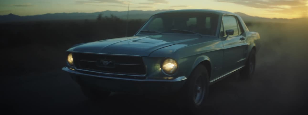 Three people ride in mustang car along road through countryside after dusk