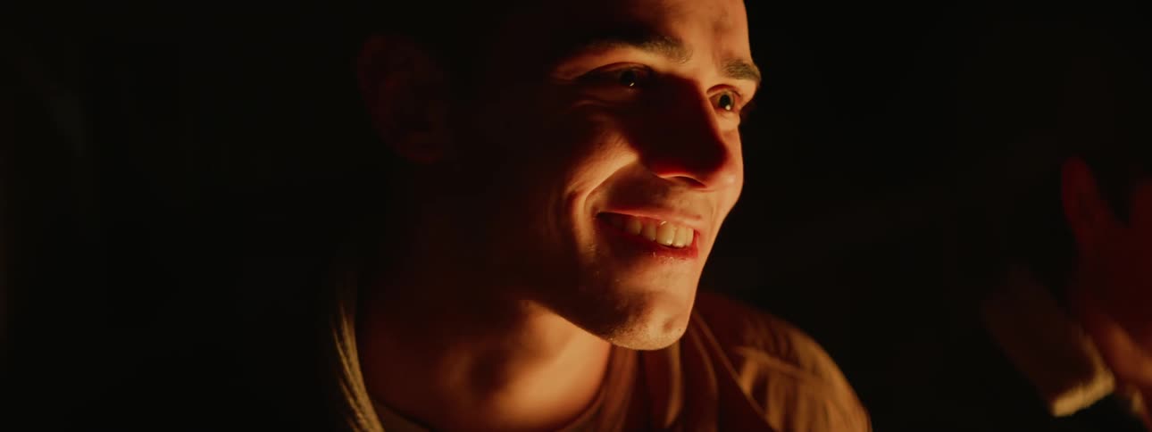 A group of friends sits around bonfire at night smiling