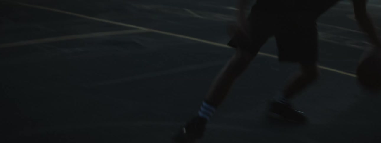 Two man playing basketball are silhouetted against the sky at dusk
