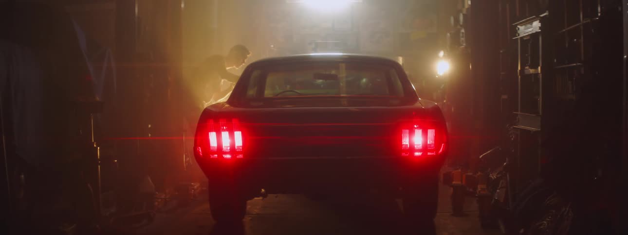 A man wiping down his car with the taillights on in a garage