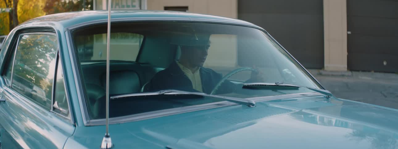 A man getting into a blue car and putting his hand on the wheel and smiling