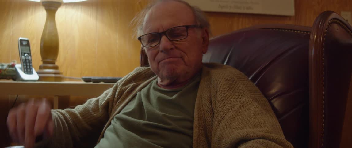 An elderly man is reading a book and sitting in a chair