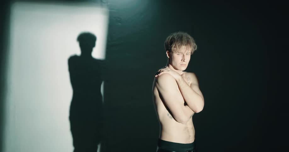 Topless shy man stands in dark room