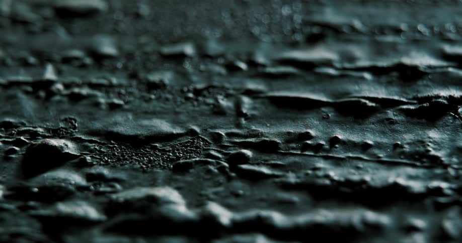 Close up of irregular surface asphalt and metal or tar at nighttime with light and shadow crossing in slow motion