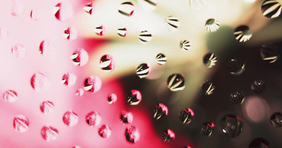 Water droplets are on clear glass as a yellow flower shaped light with red background moves behind them