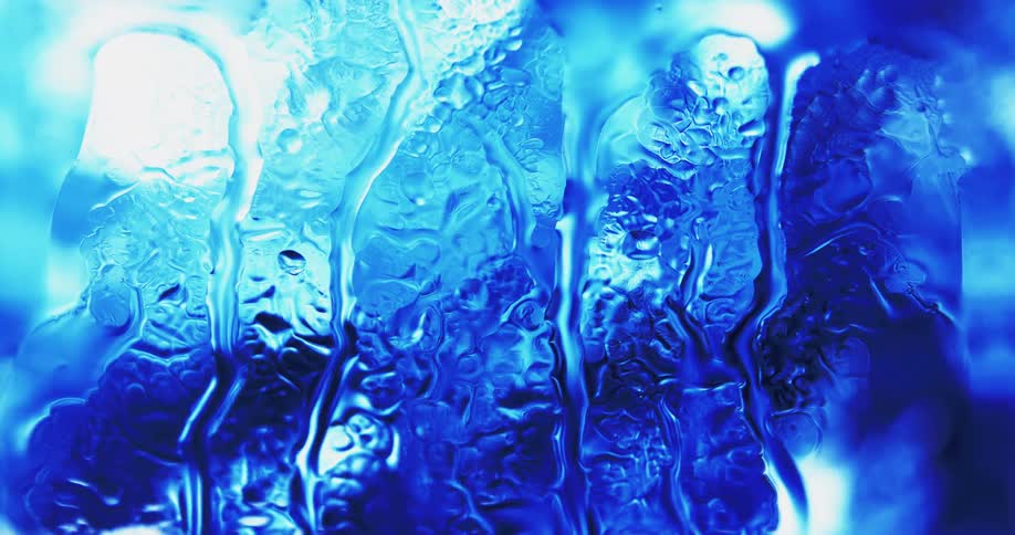 Water splashes and drips down clear glass as blue lights shine and reflects on the water