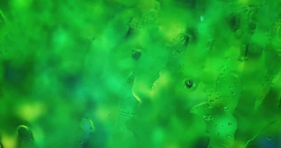 Close up of green liquid flowing behind the glass with water droplets