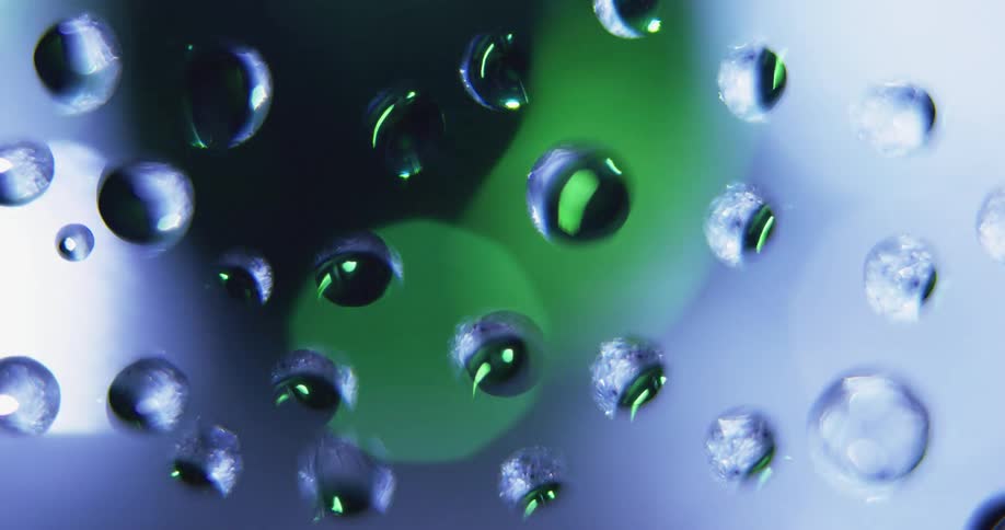 Extreme closeup of water or clear resin droplets on glass with white and green light rotating behind it