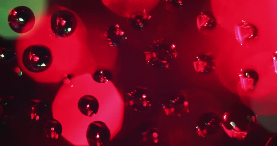 Water droplets sit on clear glass as round colored lights move in the distance reflecting light and shadows on the drops
